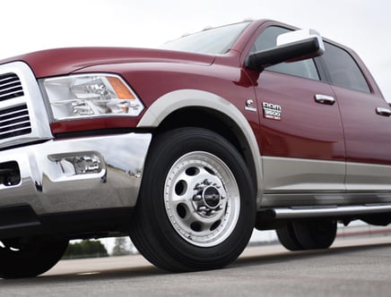 Close-up view of the front side of a red and silver Dodge Ram 3500 Heavy Duty pickup truck, focusing on the front wheel and chrome bumper.