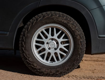 Close-up of a car's wheel featuring a multi-spoke alloy rim and a Falken Wildpeak tire on a sandy surface.