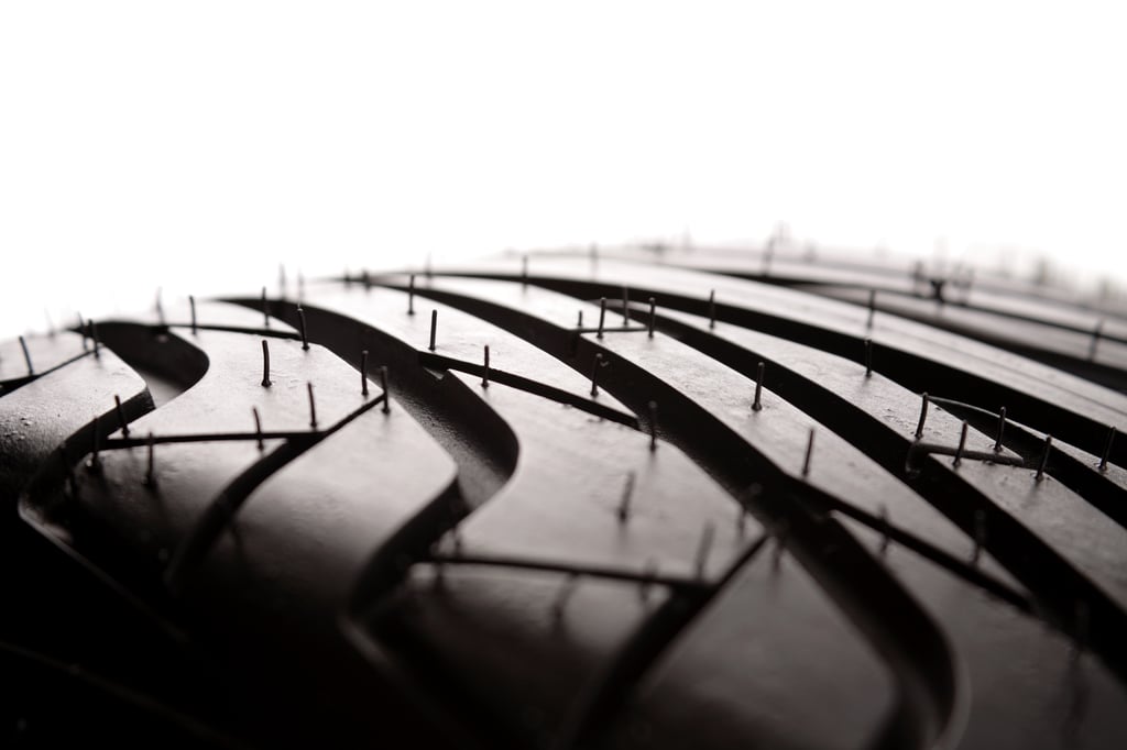 Close-up of a new tire tread with intricate patterns and small rubber spikes, against a white background.