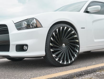 Close-up of the front end of a white car with large black and silver custom wheels, parked on a road with a yellow line visible.