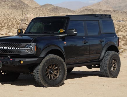 A black Ford Bronco with off-road tires parked in a desert landscape, with mountains in the background.