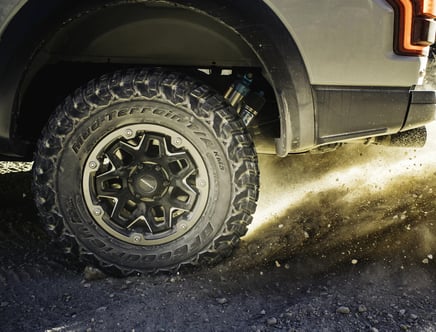 Off-road vehicle tire kicking up dirt and gravel.