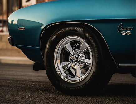 Close-up of the front wheel and fender of a classic blue Chevrolet Camaro SS, featuring chrome rims and Pantera tire branding.
