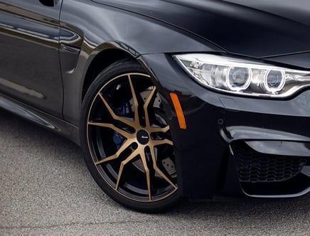 Close-up of a black car featuring a sleek design with distinctive headlights and gold alloy wheels, parked on a pavement.