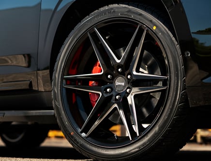 Close-up of a car's wheel with a stylish black and silver rim and red brake calipers.