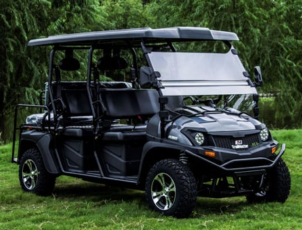 A black TrailMaster 800 electric utility vehicle with an open roof and two bench seats, parked on a grassy area surrounded by trees.