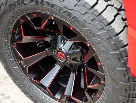 Close-up of a tire with a black and red custom rim featuring intricate design and visible text on the tire's surface.