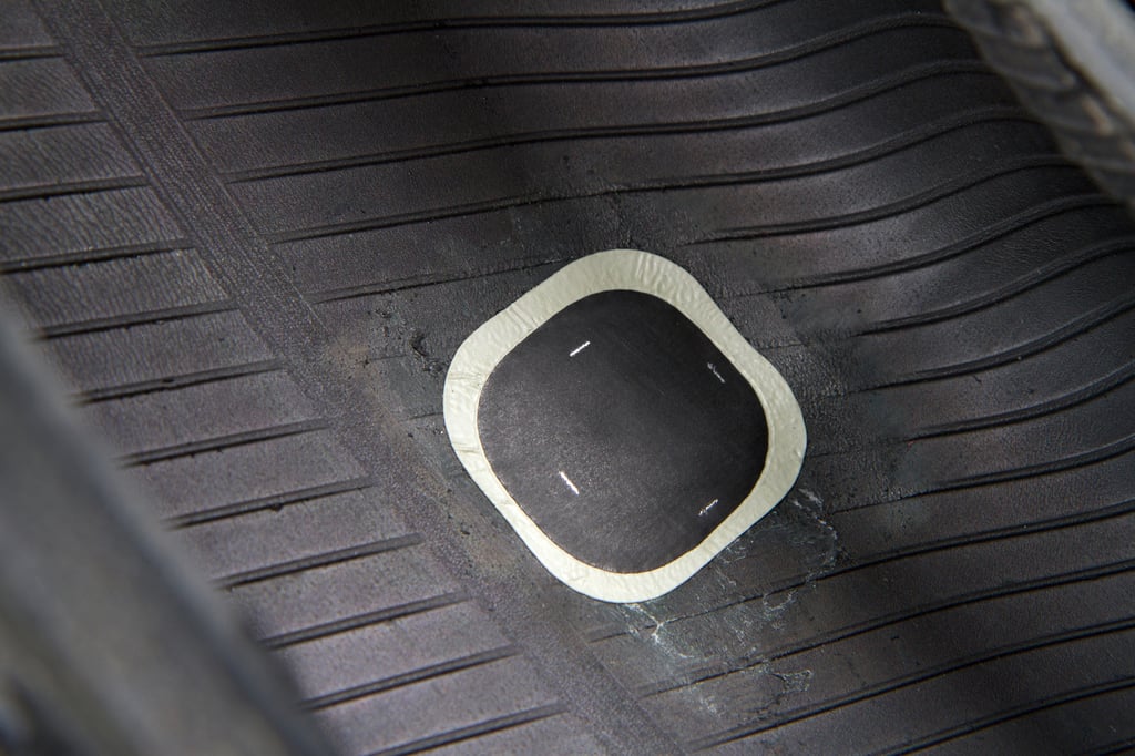 A tire patch is applied to the inside of a rubber tire, showing a smooth black surface with a rounded, square-shaped patch in the center, secured with a white adhesive edge.