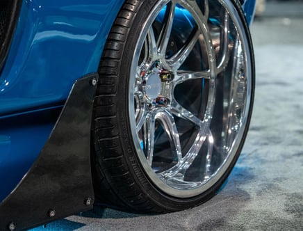 Close-up of a low-profile car tire with shiny chrome alloy rims, fitted on a blue vehicle with a black carbon fiber side skirt.