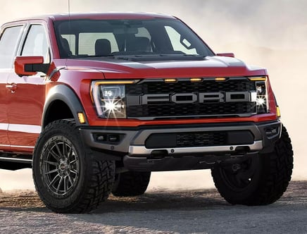 A red Ford pickup truck with rugged tires and a bold front grille parked on a sandy terrain.