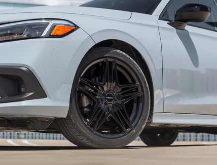Close-up of the front wheel of a white car with stylish black alloy rims and a side mirror, showcasing the headlights and part of the front bumper.
