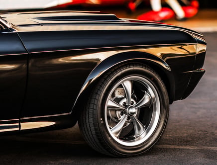 Close-up of the front wheel and fender of a classic black car with shiny silver rims and a smooth, glossy finish.