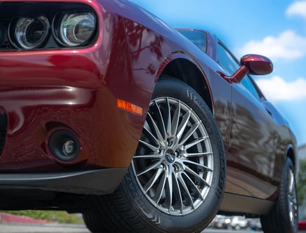 Low-angle view of a red sports car focusing on the front wheel and grille, with a clear blue sky in the background.