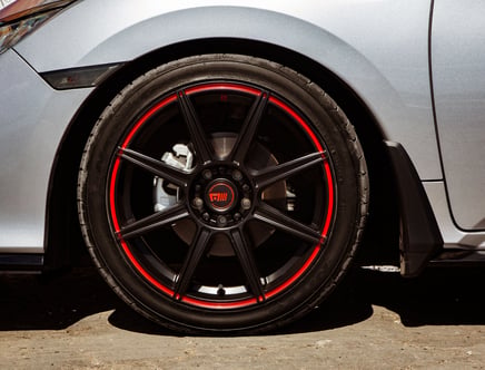 Close-up view of a car's black alloy wheel with red accents, mounted on a silver vehicle.