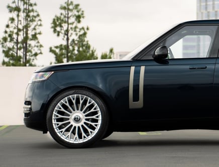 Side view of a black luxury SUV featuring a distinctive silver trim and large custom alloy wheels, parked outdoors with trees and buildings in the background.