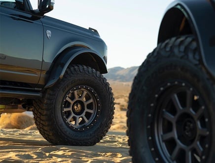 Close-up of the wheels of two off-road vehicles with large, rugged tires on a sandy desert terrain.