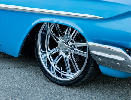 Close-up of a blue car with chrome wheels and a shiny silver trim, parked on a paved surface.