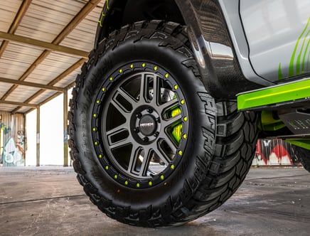 Close-up of a rugged off-road tire on a vehicle, featuring a black wheel rim with yellow accents, set in an industrial environment.
