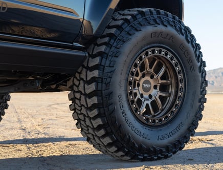Close-up of an off-road vehicle tire with rugged tread, labeled 'Baja Boss,' mounted on a vehicle in a desert setting.