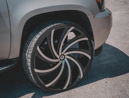 Close-up of a car's large, stylish alloy wheel with black and silver swirl design, parked on pavement.
