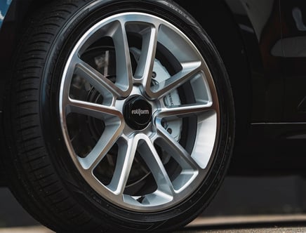 Close-up of a car wheel featuring a Rotiform alloy rim with a modern multi-spoke design and a small black center cap, situated on a dark tire with visible treads against a black vehicle body.