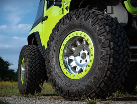 Close-up view of a bright green off-road vehicle with large, rugged tires on a gravel path, against a blue sky background.