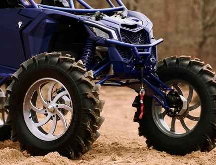 Close-up of a blue off-road vehicle with large, rugged tires and metal rims on a sandy terrain.
