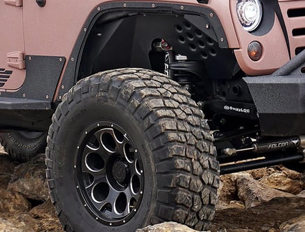 Close-up of a rugged off-road vehicle's front wheel with large, chunky tires on rocky terrain.