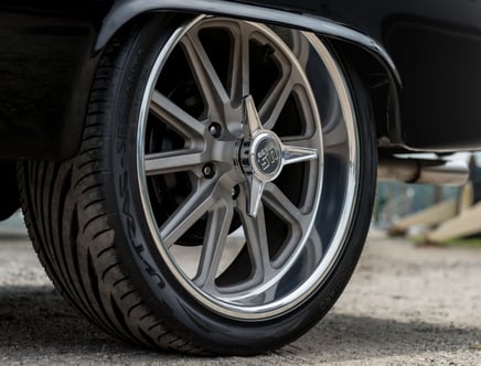 Close-up of a car's wheel featuring a shiny metallic rim with a star-shaped centerpiece and a Vredestein Ultrac Sessanta tire, on a black vehicle parked on gravel.