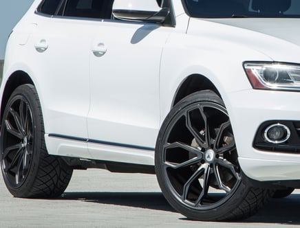 Close-up of a white SUV with large black alloy wheels on a concrete pavement.