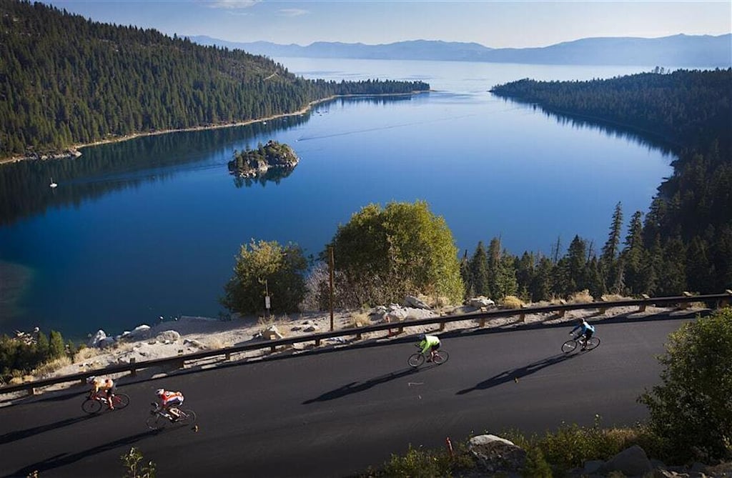 A wide view of Lake Taho and four cyclists cycling by the shoreline.