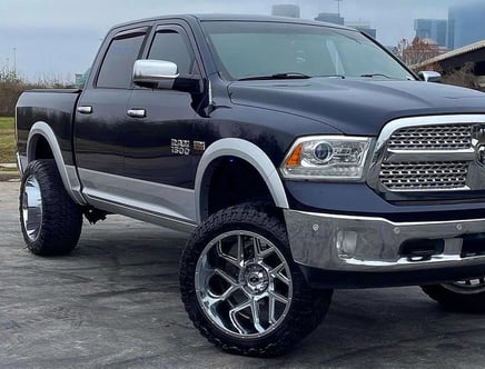A black Ram 1500 pickup truck with chrome accents and large custom wheels parked on a concrete surface.