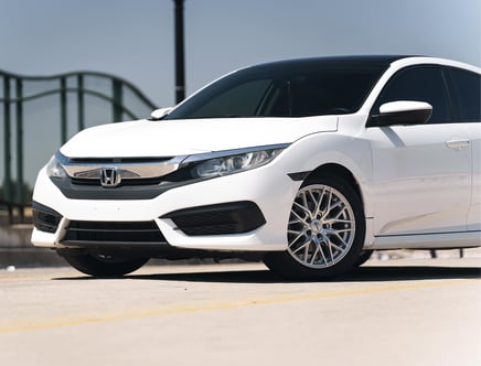 White Honda sedan parked on a concrete surface, featuring a sleek front design and alloy wheels, with a metal railing in the background.