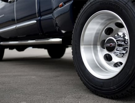 Close-up of a shiny silver truck wheel with a Vision branding, mounted on a vehicle parked on a paved surface.