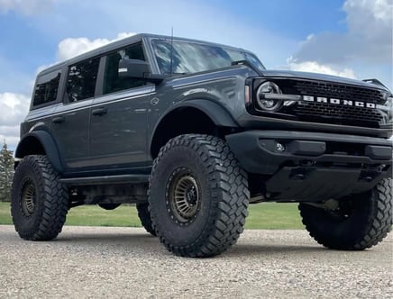 A gray off-road vehicle with large, rugged tires and a prominent front grille, parked on a gravel surface with a cloudy blue sky in the background.