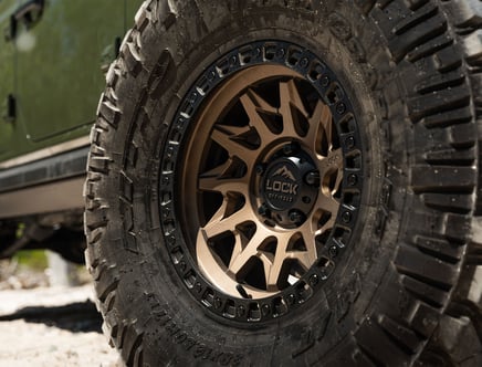 Close-up of an off-road vehicle wheel, featuring a rugged tire with deep treads and a bronze-colored alloy wheel labeled 'LOCK OFF-ROAD.'