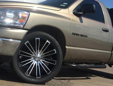 Close-up of the front passenger side of a tan Ram 1500 truck, featuring large, custom chrome and black wheels, and the truck's logo on the door.