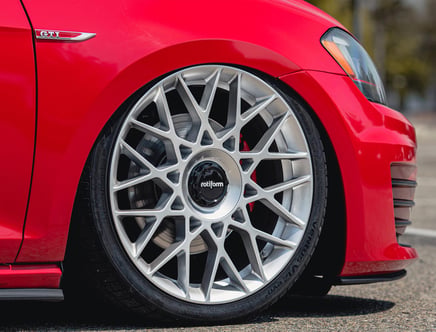 Close-up of a red car featuring a silver Rotiform alloy wheel with a multi-spoke design and a GTI badge on the fender.