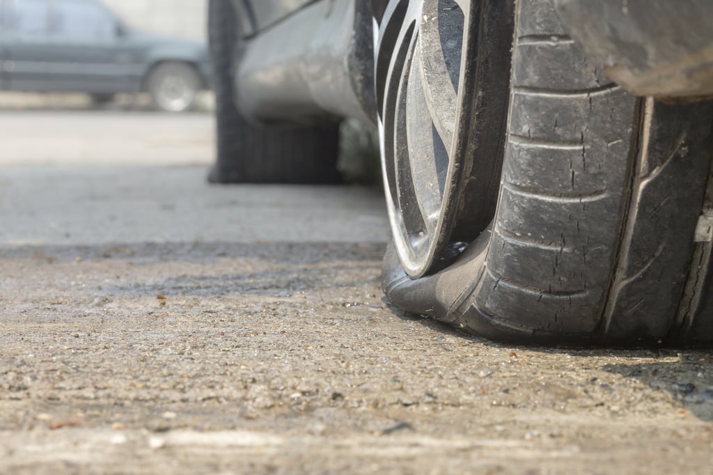 Closeup of the driver's side of a vehicle with two flat tires, the rear one shows not only very little tread depth but also evidence of dry rot and tread separation.