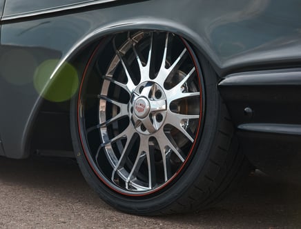 Close-up of a reflective chrome car wheel with a multi-spoke design and a tire on a vehicle, featuring a red accent ring and a 'U.S. Mags' logo at the center.