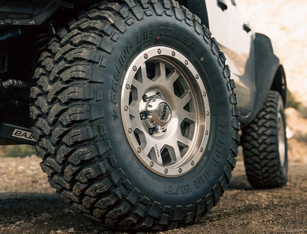 Close-up of a rugged off-road vehicle tire with deep tread patterns on a gravel surface.
