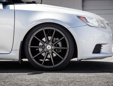 Close-up of a silver car featuring a black multi-spoke wheel, parked on a paved surface.
