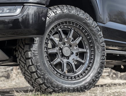 Close-up of a rugged off-road tire mounted on a black vehicle, showcasing detailed tread patterns and a metallic wheel design.