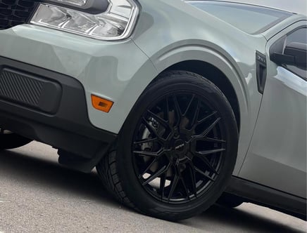 Close-up of the front end of a gray vehicle featuring a modern headlight, an orange reflector, and a black multi-spoke wheel with the word 'AUDITION' on the center cap.