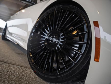 Close-up of a black, multi-spoke alloy wheel on a white car, highlighting the intricate design and glossy finish.