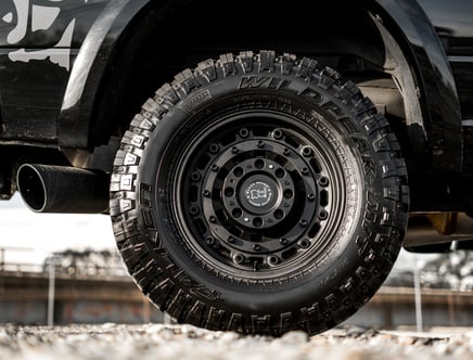 Close-up of a rugged off-road tire labeled "WILDPEAK" on a black vehicle, with emphasis on the black alloy wheel and textured tread pattern.