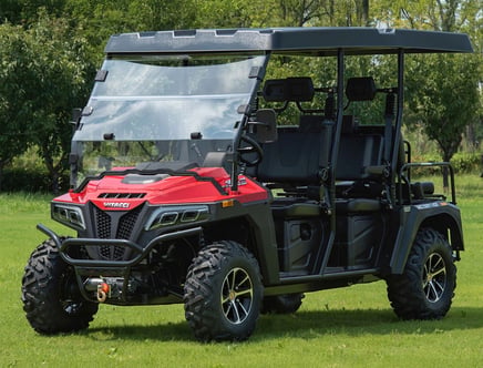 A red Vitacci all-terrain vehicle (ATV) with a transparent windshield and a roof, parked on grass with trees in the background. The vehicle features large off-road tires and seating for multiple passengers.