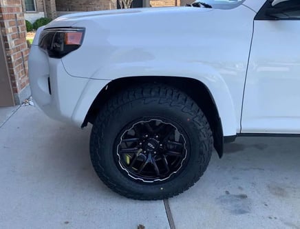 Front side view of a white SUV with a focus on its black alloy wheel, parked on a driveway.