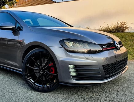 Front side view of a silver Volkswagen GTI with black wheels and red brake calipers, parked on a street.